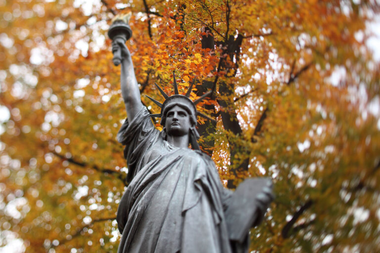 The Statue of Liberty in Paris in front of bright fall foliage.