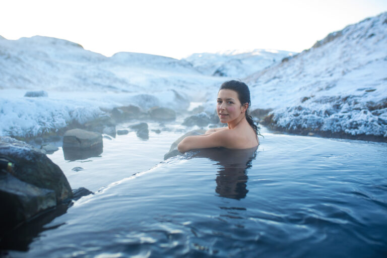 A woman rests her elbows on the edge while she stands in a hot spring.