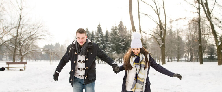 A warm-dressed couple traipses through the snow.