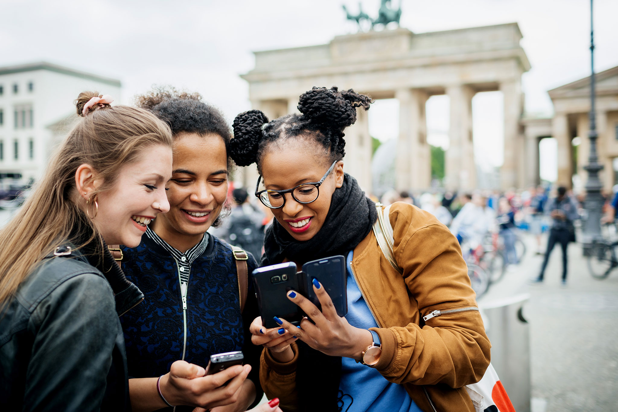 Three young women visiting Berlin stop to look over recent photos on their phones.