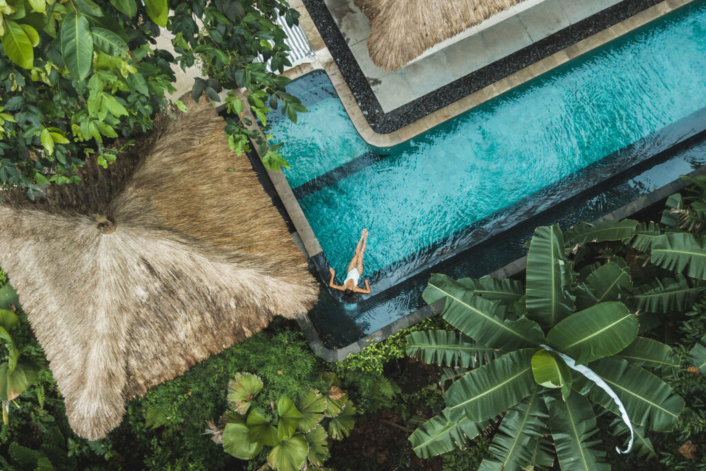 Aerial view of a woman lounging in a pool amid tropical foliage.