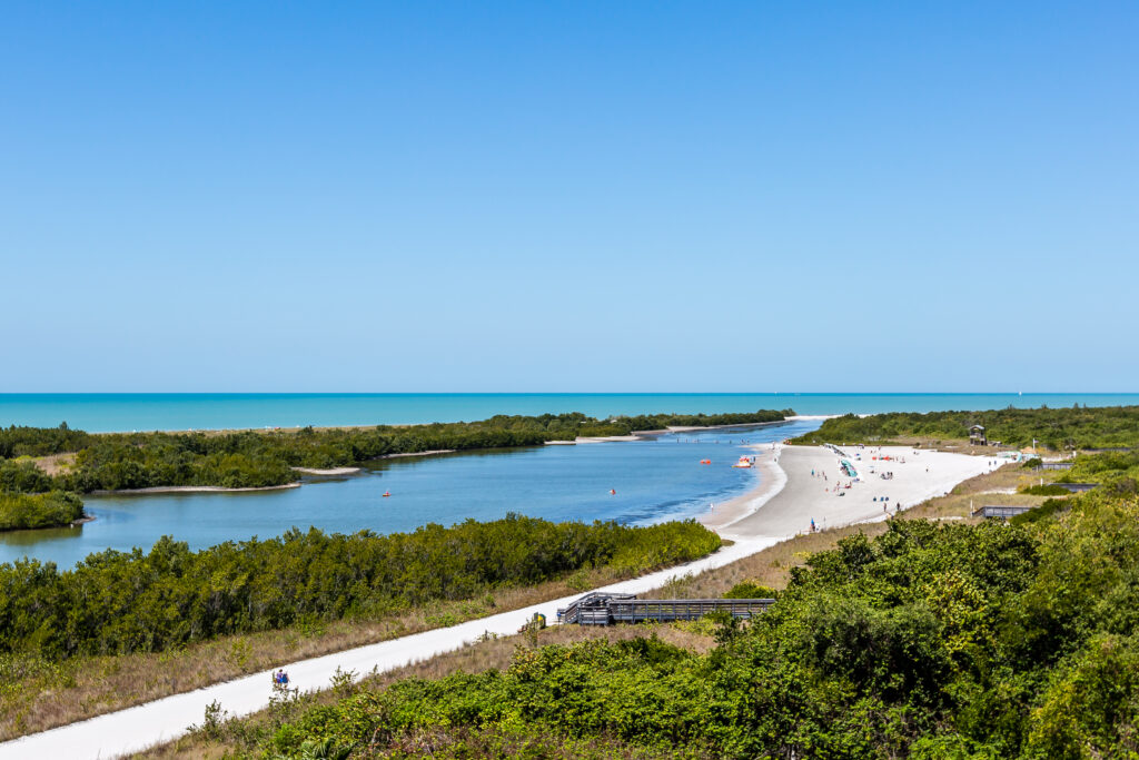 Aerial view of a coastal lagoon and sandy beach bordered by lush greenery and turquoise water under a clear blue sky.