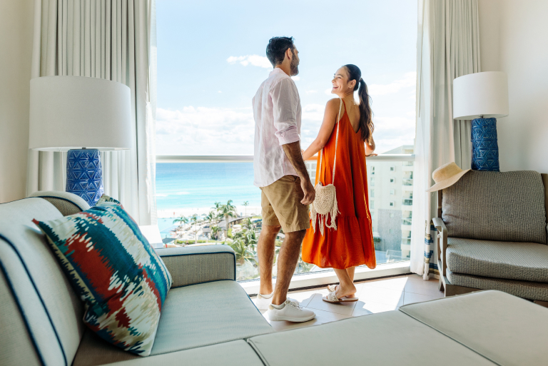 Guests enjoy ocean views from a bright resort suite with floor-to-ceiling windows.